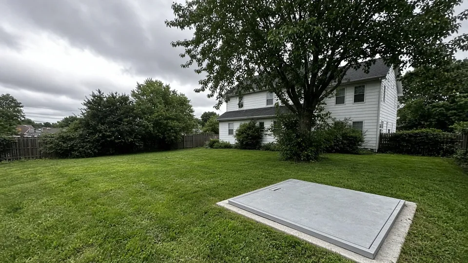 Flush steel storm shelter door in the lawn behind a brick home in Indiana